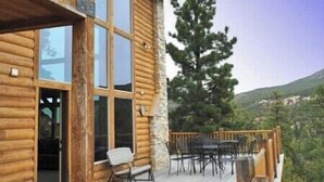 Une cabane en bois dotée d’une terrasse, de grandes fenêtres et d’une cheminée en pierre.