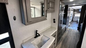 A modern RV interior with a kitchen area featuring a sink, cabinets, and a large mirror.