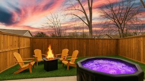 Un jardin avec un jacuzzi, un foyer et des chaises en bois.