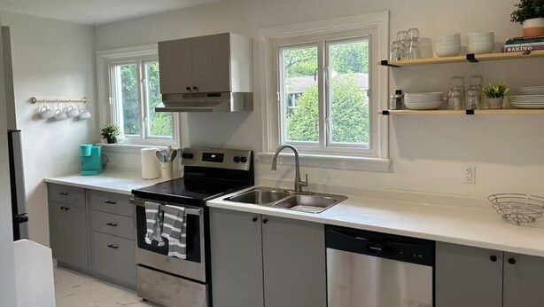 A modern kitchen with stainless steel appliances, a double sink, and a window providing natural light. - South End Bungalow - 5 full bedrooms (Greater Sudbury)