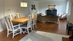 A dining area with a wooden table and white chairs, a dark-colored sofa, and a fireplace. - South End Bungalow - 5 full bedrooms (Greater Sudbury)