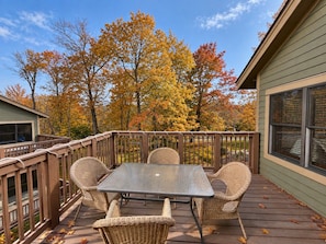 A deck with a table and chairs, surrounded by a wooden railing, overlooking a garden with autumn foliage.