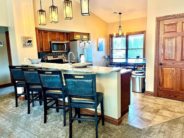 A kitchen with a central island, bar stools, wooden cabinets, a microwave, and a refrigerator.