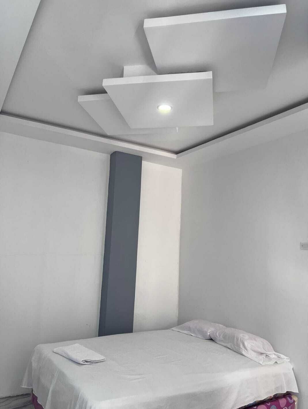 Een moderne slaapkamer met een bed, een witte muur en een plafondlamp.
