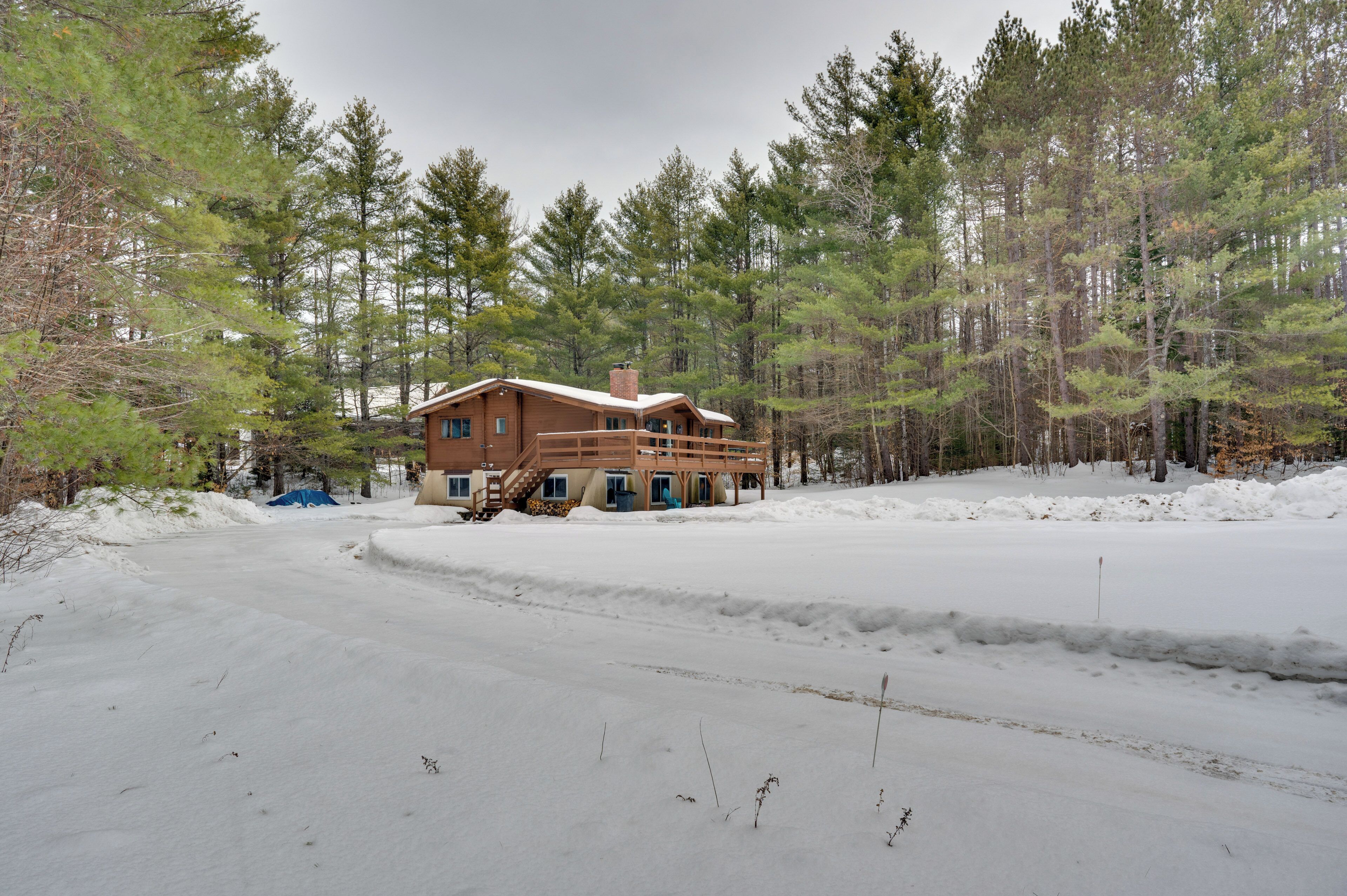Una cabaña con terraza de madera y porche cubierto, rodeada de bosque y nieve.