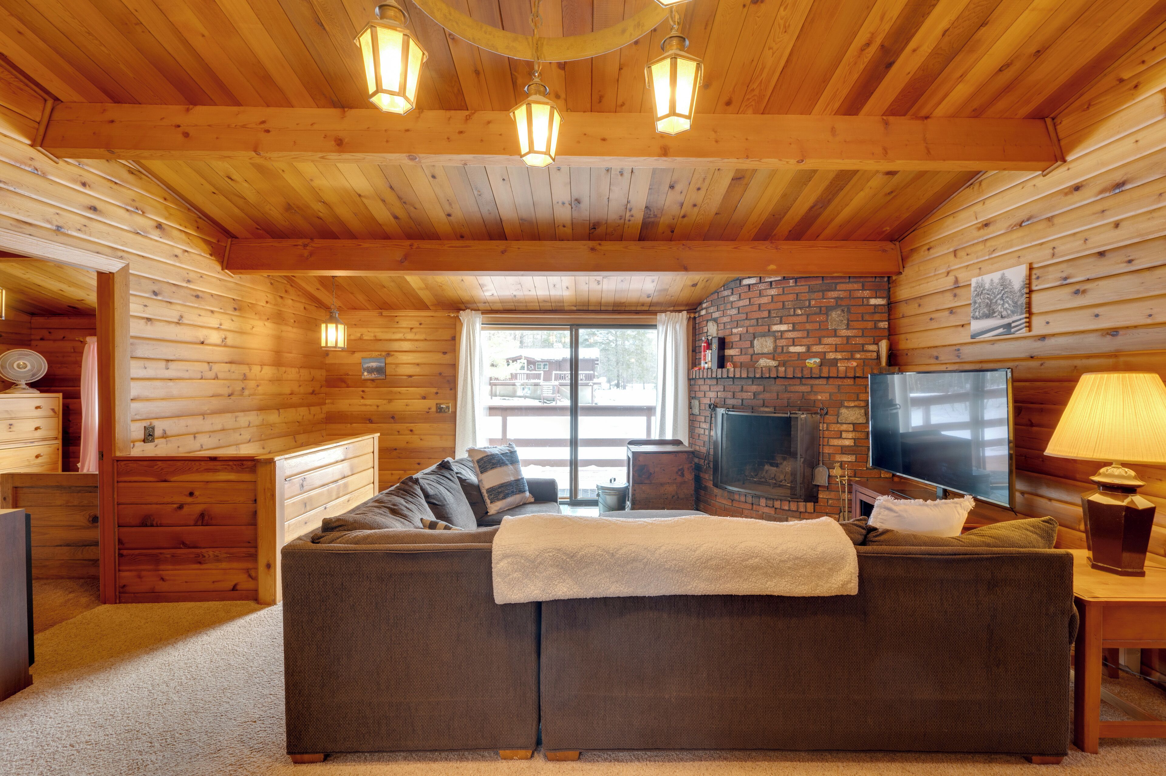 L’intérieur d’une cabane en rondins, avec un plafond en bois, une cheminée en briques, un canapé, un téléviseur et une lampe.