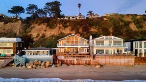 A beachfront property with a wooden deck, a large house with a balcony, and a smaller building with a staircase. - Unbeatable Beachfront Bliss w/ Ocean Views, Luxe Interiors & Patio Beach Road (Dana Point)