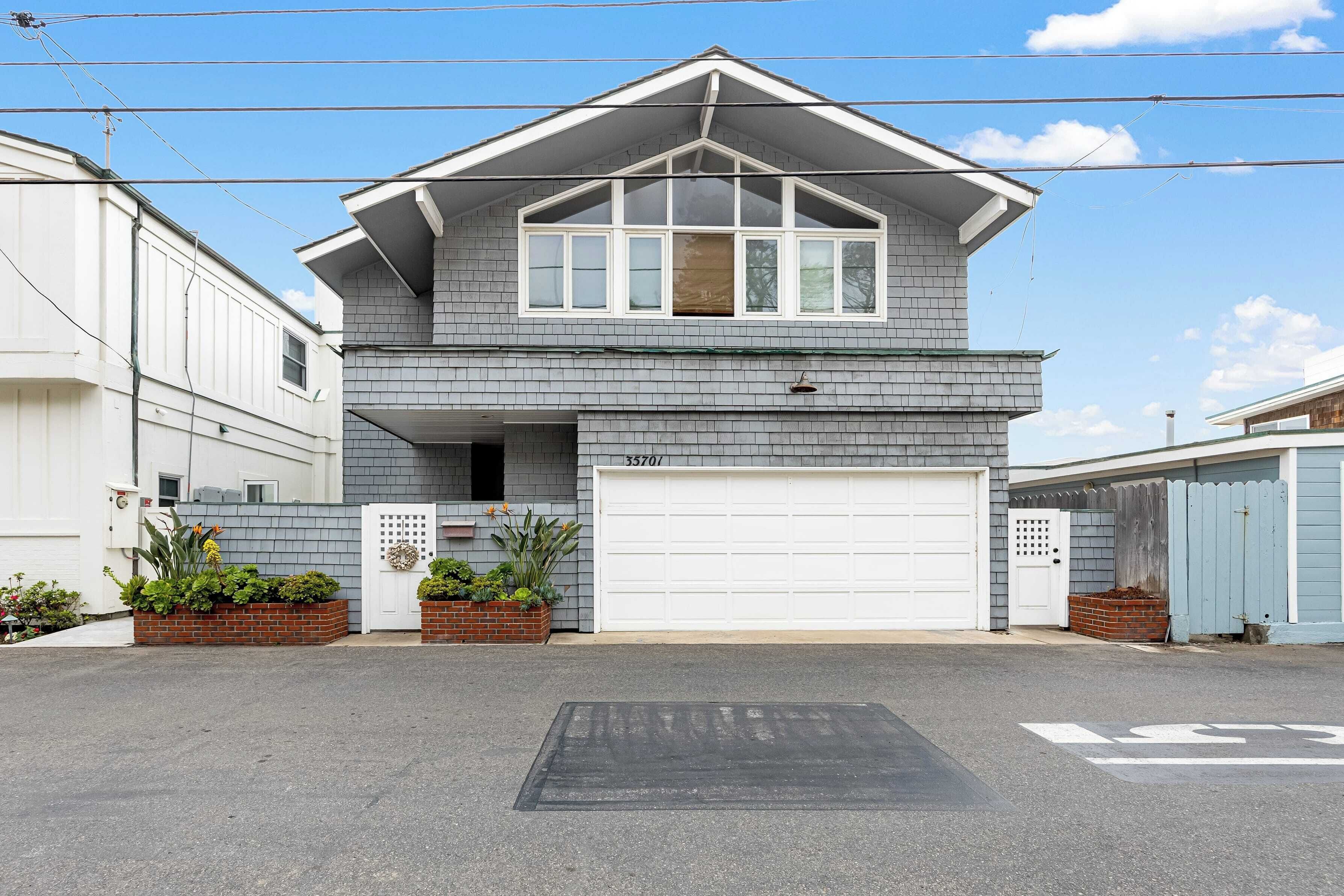 Une maison à deux étages avec un garage, une véranda ornée de plantes et un ciel dégagé.