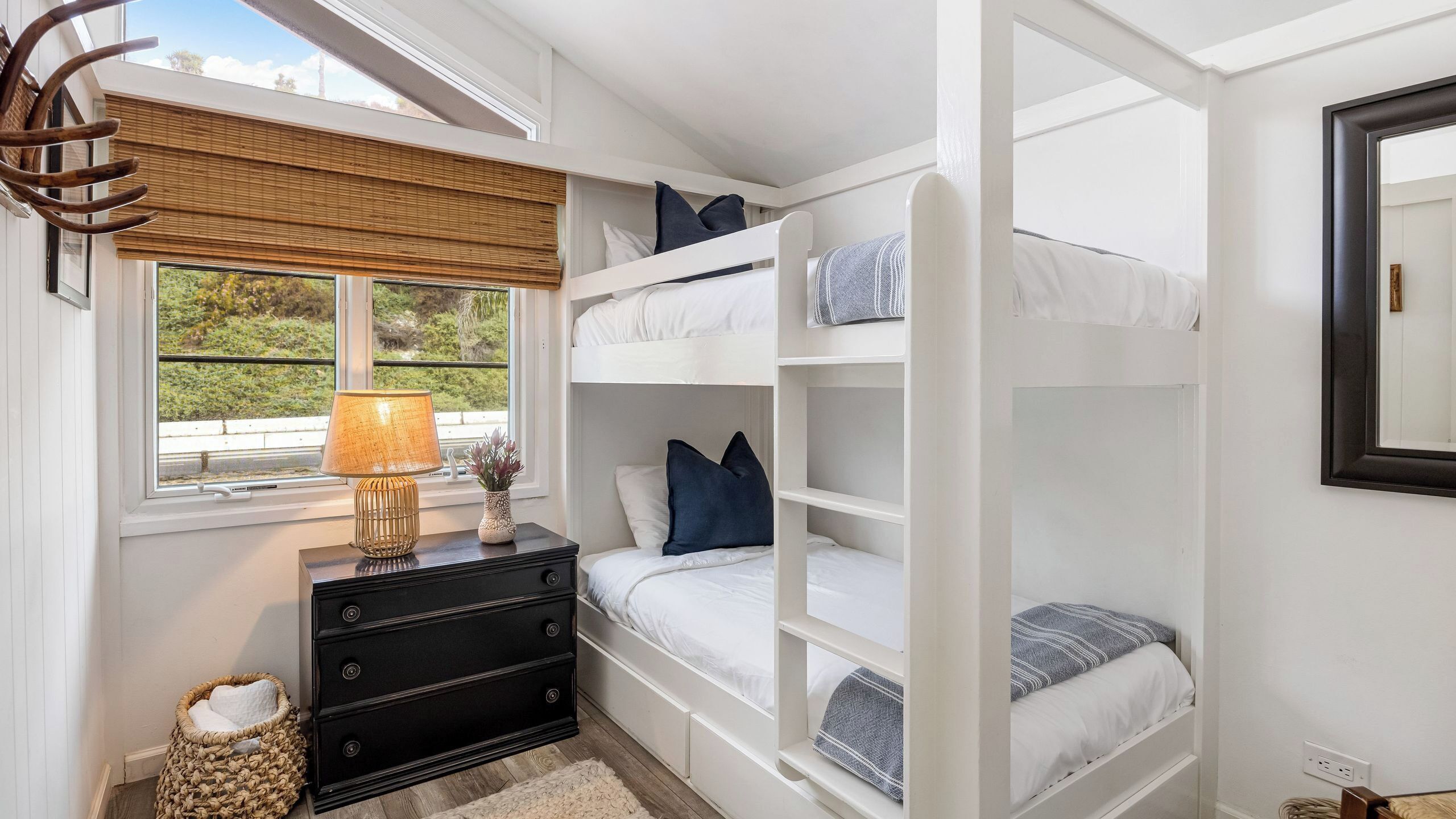 Een slaapkamer met een stapelbed, een raam, een dressoir en een lamp.