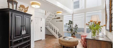 A spacious room with a high ceiling, a staircase, a large wooden cabinet, and a potted plant.