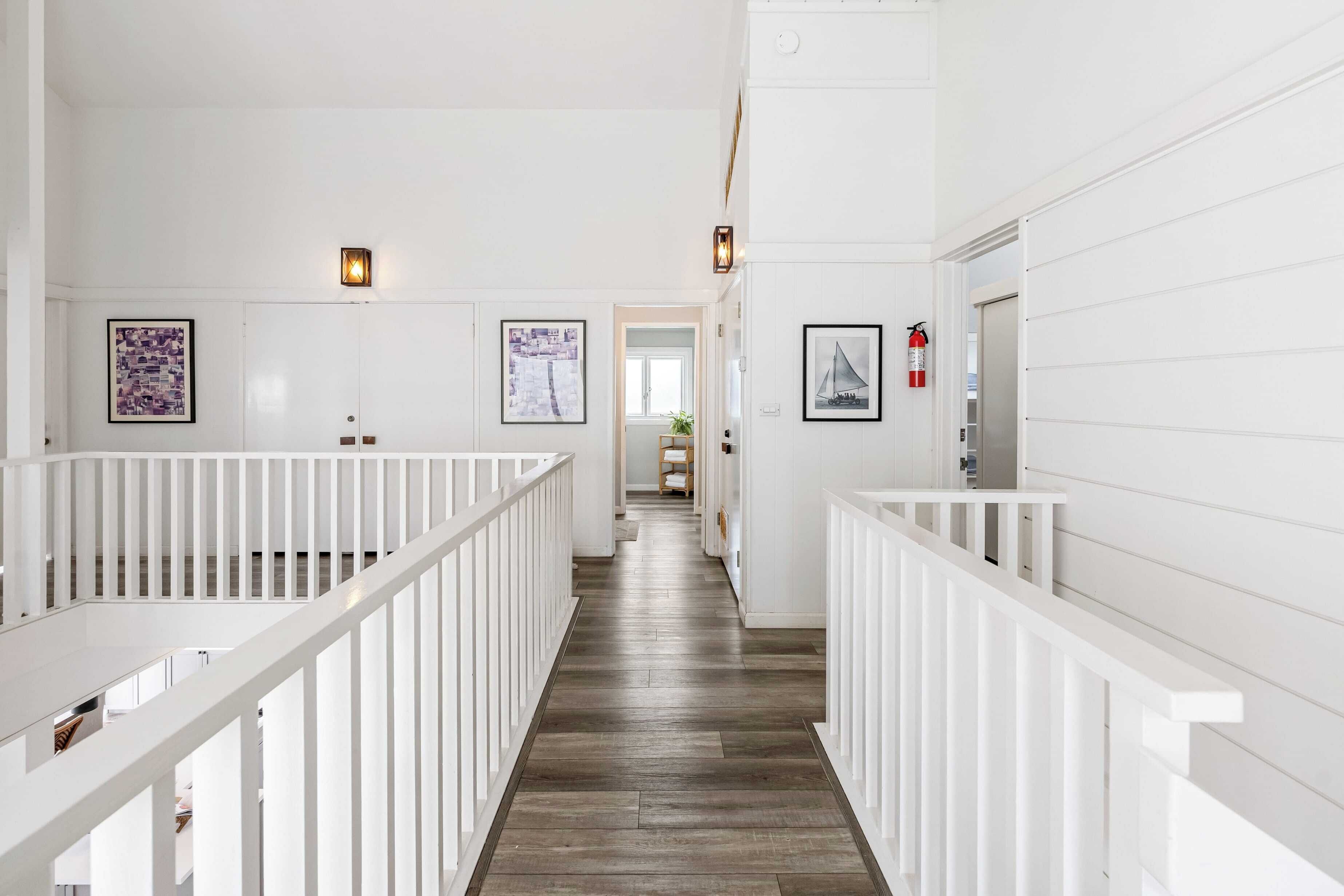 A hallway with white railings, wooden flooring, and framed artwork on the walls.