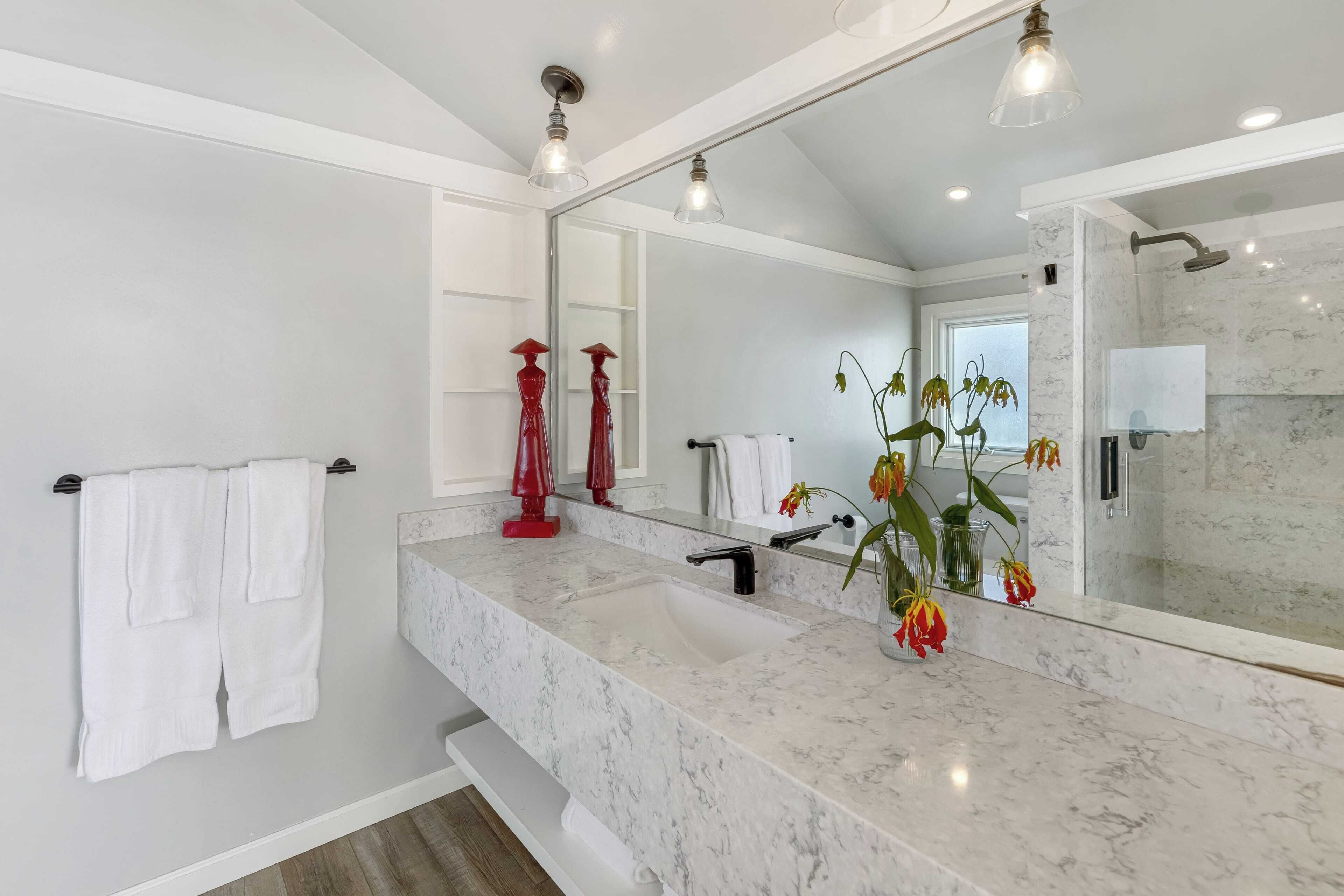 Un baño moderno con un lavabo de mármol, un espejo grande y una zona de ducha.