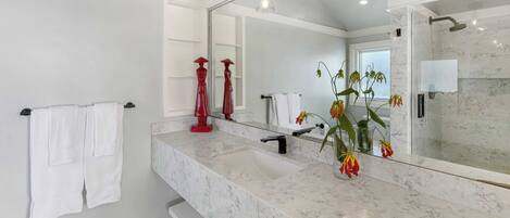 Un baño moderno con un lavabo de mármol, un espejo grande y una zona de ducha.