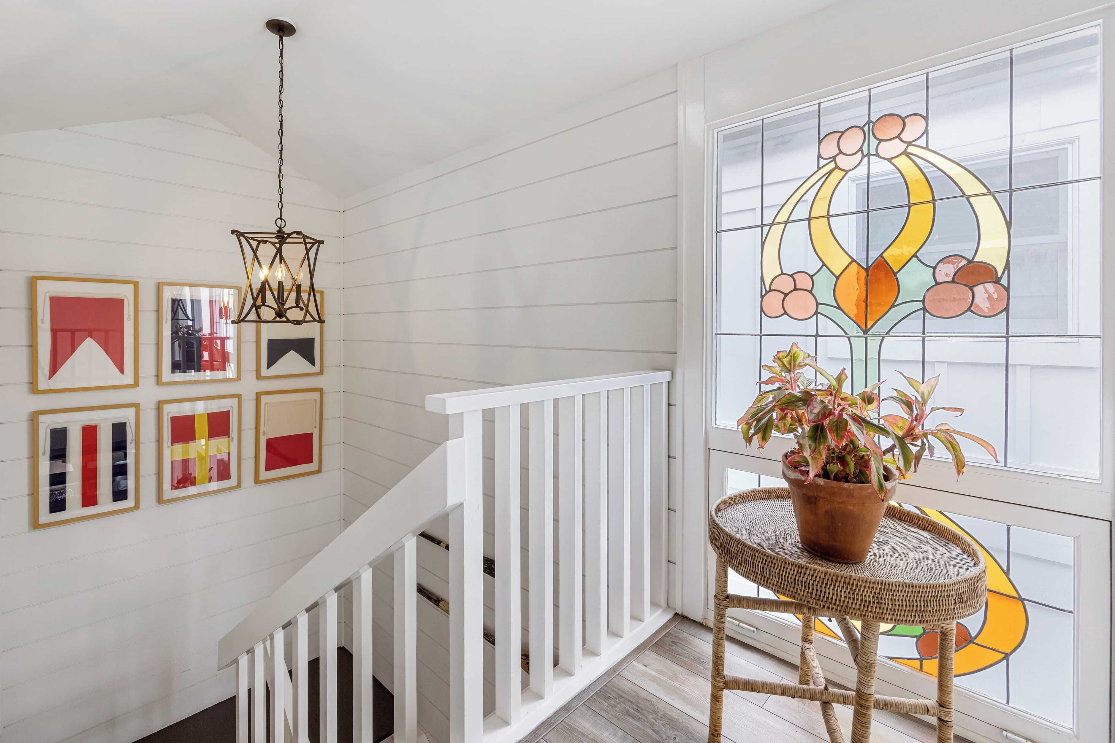 A staircase with white railings leading to a room with a large stained glass window and a potted plant on a wicker table.