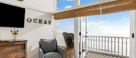 A room with a TV, a dresser, a chair, a wicker basket, and a view of the ocean.