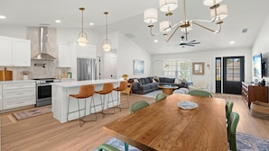A modern kitchen with white cabinets, a central island, and a dining area with a wooden table and green chairs.