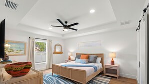 A bedroom with a bed, bedside tables, a ceiling fan, a window with curtains, a wall-mounted mirror, and a view of the outdoors.