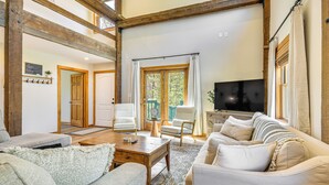 Un salón amplio con techo de madera, un televisor grande y asientos cómodos, incluyendo un sofá y sillones.