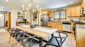 Una cocina moderna con armarios de madera, un refrigerador de acero inoxidable y un comedor con mesa de madera y sillas negras.