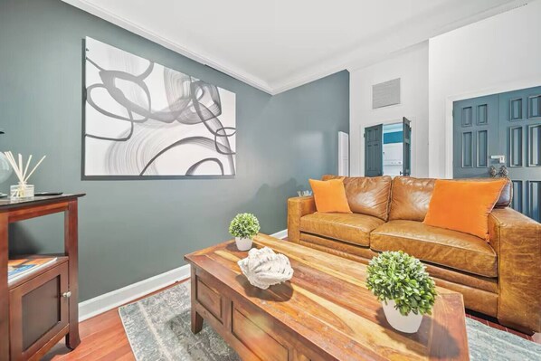 A living room with a brown leather sofa, wooden coffee table, and a large abstract painting on the wall.