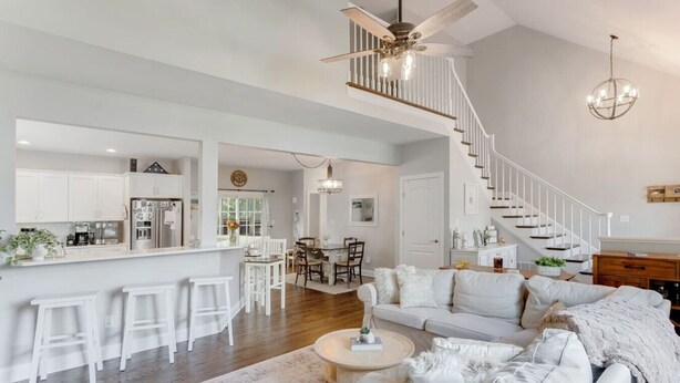 A spacious living area with a high ceiling, a staircase, a kitchen, and a dining area. - Captains Quarters in Charming Lewes! (Lewes)