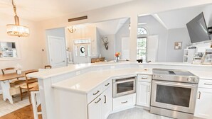 A modern kitchen with white cabinetry, stainless steel appliances, and a large island. - Captains Quarters in Charming Lewes! (Lewes)