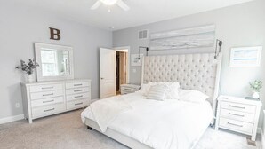 A bedroom with a large bed, a dresser, a nightstand, a ceiling fan, and a painting on the wall. - Captains Quarters in Charming Lewes! (Lewes)