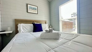 Un lit bien fait, avec une literie blanche, un oreiller bleu et une étoile de mer en guise de décoration sur la table de chevet.