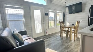 Une cuisine moderne avec un coin repas, comprenant une table et des chaises en bois, un canapé en cuir noir et un téléviseur à écran plat fixé au mur.