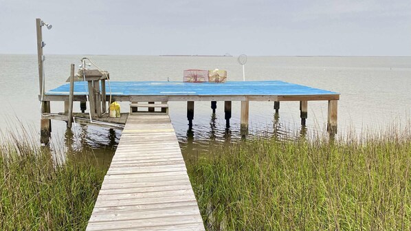 Une jetée en bois s’étendant dans une étendue d’eau calme, avec une structure dotée d’un toit bleu à son extrémité.
