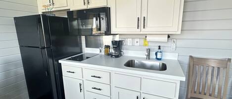 A kitchen with white cabinets, a black refrigerator, a stainless steel sink, and a coffee maker.