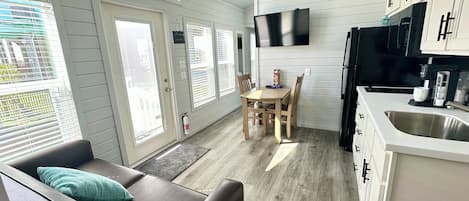 Una cocina moderna con comedor, un sofá con un cojín azul verdoso y un televisor montado en la pared.