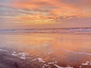 A beach with waves gently lapping at the shore under a sunset sky.