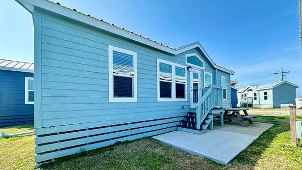 A light blue wooden house with a porch, a small deck, and a concrete pathway leading to the entrance.
