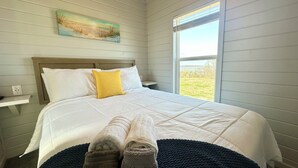 A bedroom with a bed, a window, and a painting on the wall.