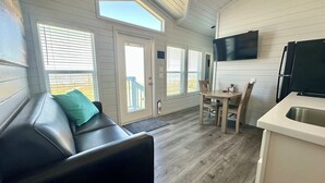 A compact living space with a sofa, a dining table with chairs, a kitchen area with a sink, and a television mounted on the wall.