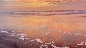 A beach with waves gently lapping at the shore under a sunset sky.