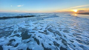 Una playa con olas y un atardecer al fondo.