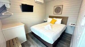 Una habitación de hotel con una cama, un televisor montado en la pared y un estante pequeño.