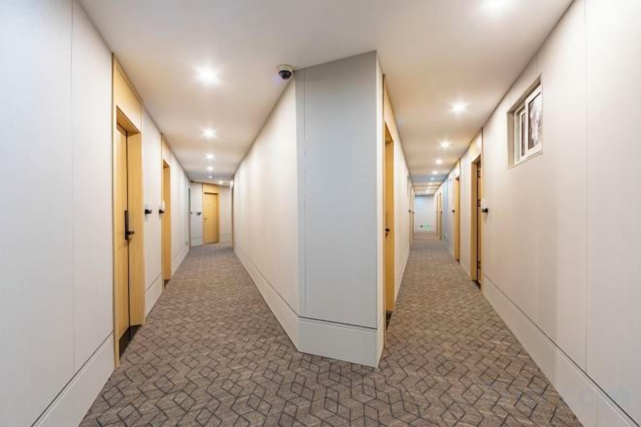 A hotel corridor with doors on both sides, a patterned carpet, and recessed lighting.
