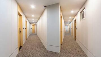 A hotel corridor with doors on both sides, a patterned carpet, and recessed lighting.