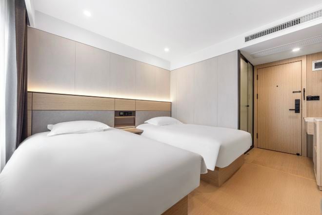 A hotel room with two beds, a wooden headboard, a bedside table, and a door.