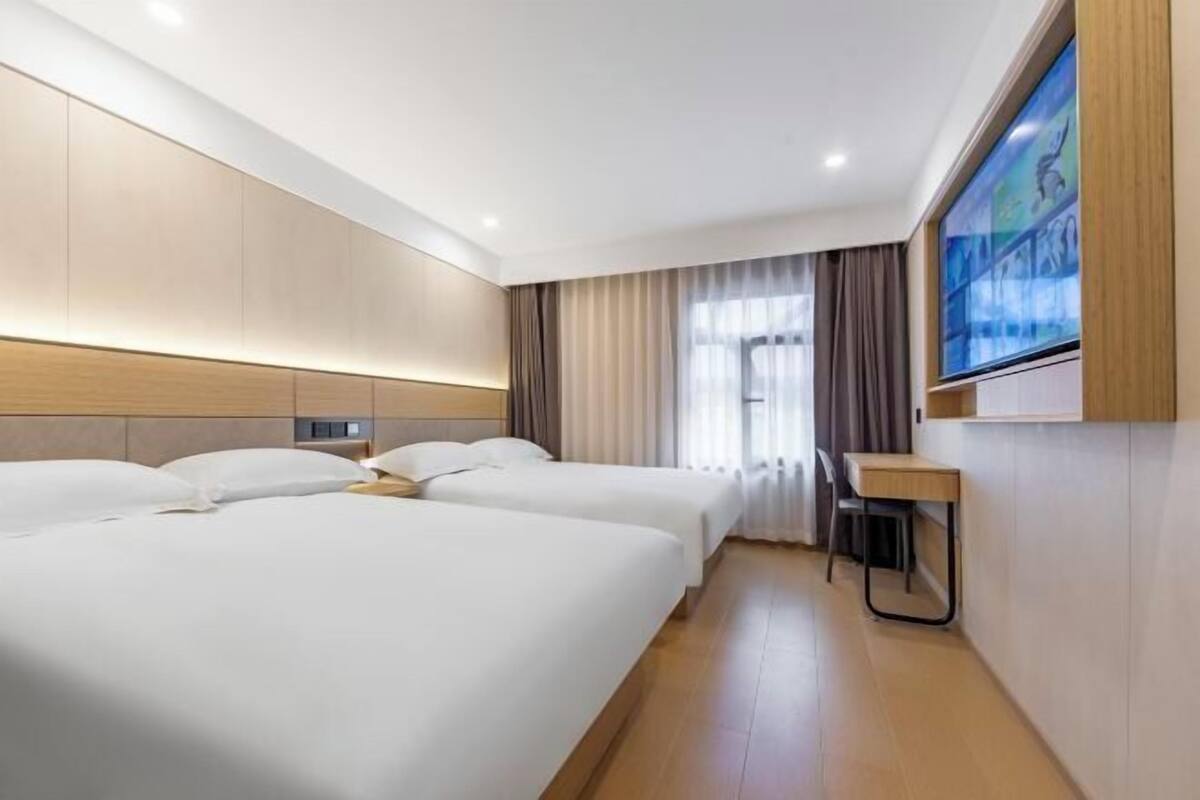 A hotel room with two beds, a desk, a TV, and a window with curtains.
