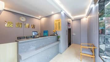 A hotel reception area with a reception desk, a clock, a menu board, and a seating area.