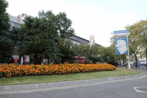 A building with a large blue sign, a flower bed, and palm trees. - Bohu Hotel (Shanghai)