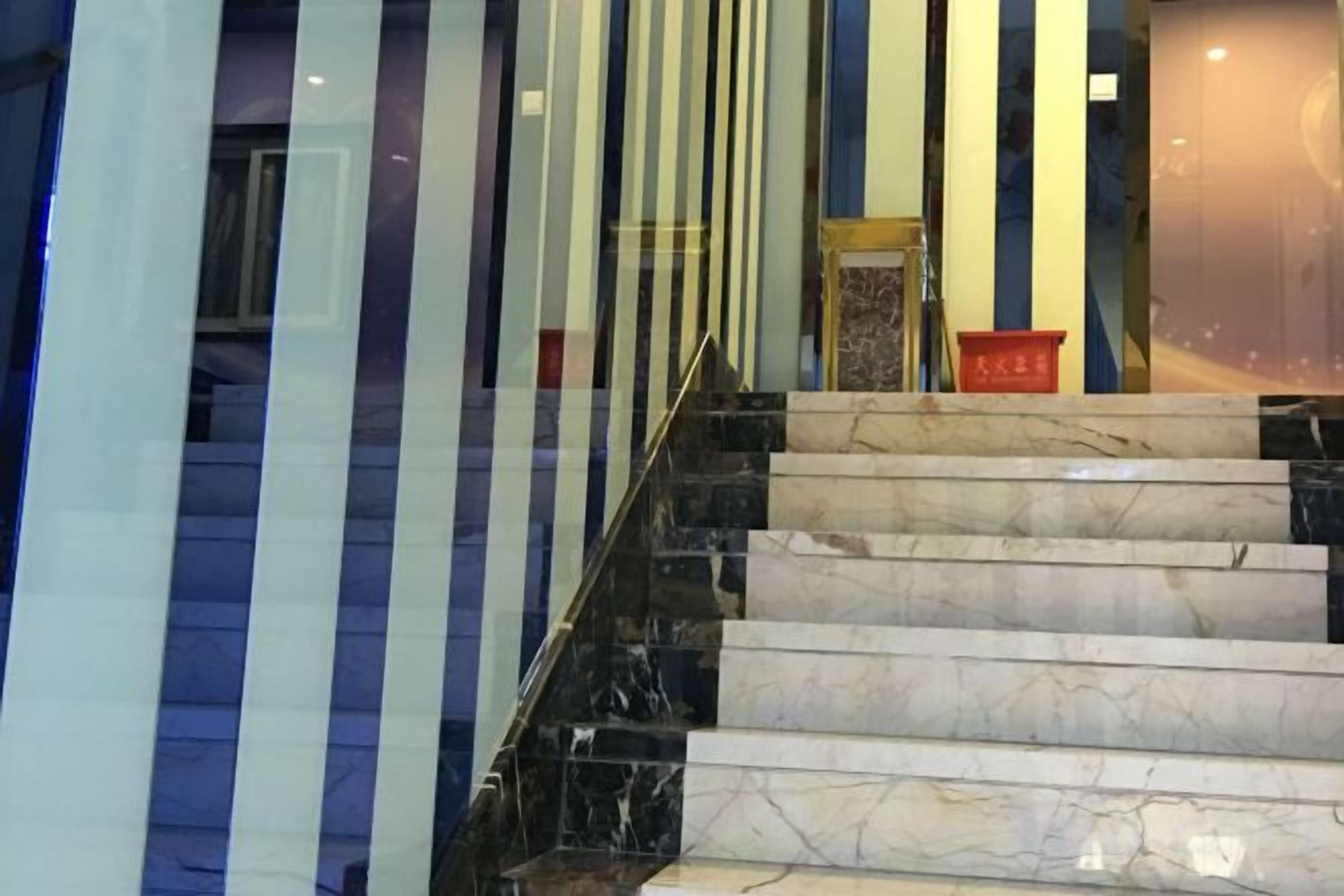 A staircase with marble steps and black railings, leading to a room with a glass wall and a red object on the floor.