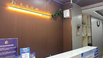 A reception desk with a wooden panel wall, a sign with text, and a reception area with shelves and a clock.