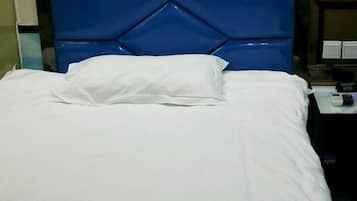A bed with a white sheet and a pillow, a blue headboard, and a bedside table with a remote control.