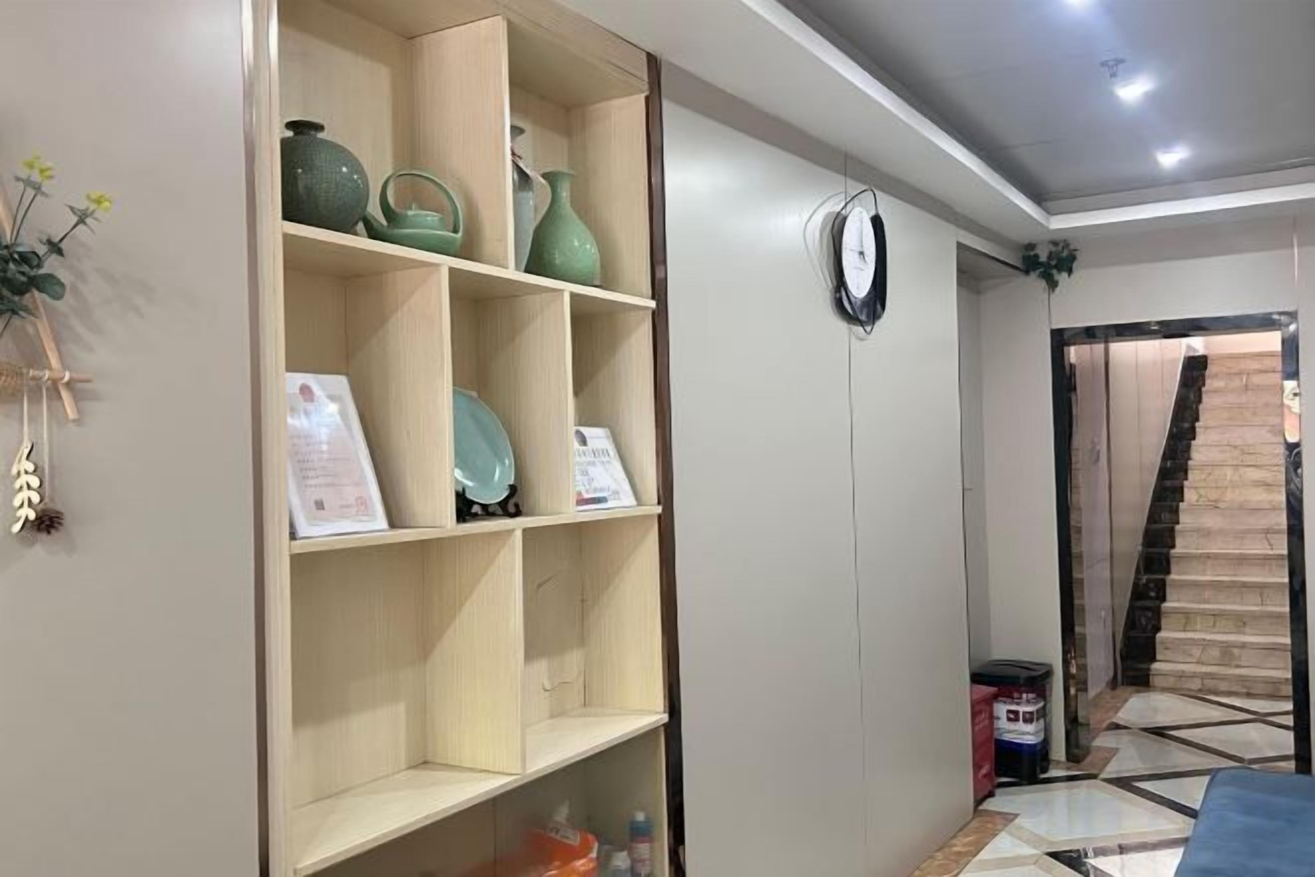 A room with a built-in shelf unit, a clock on the wall, and a tiled floor.