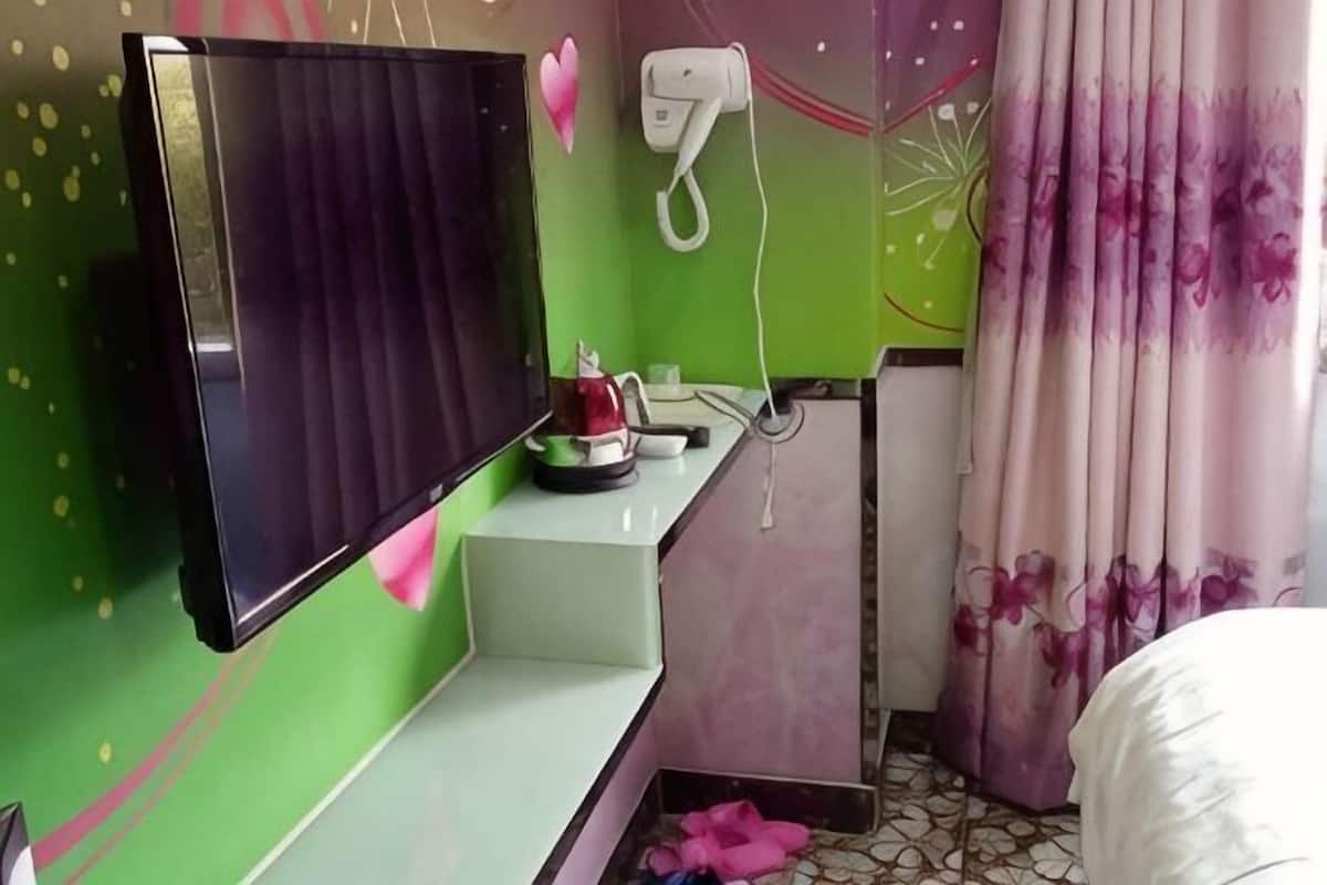 Une chambre dotée d’une télévision à écran plat, d’une petite table avec une bouilloire, d’un sèche-cheveux et d’un lit recouvert d’une couverture blanche.
